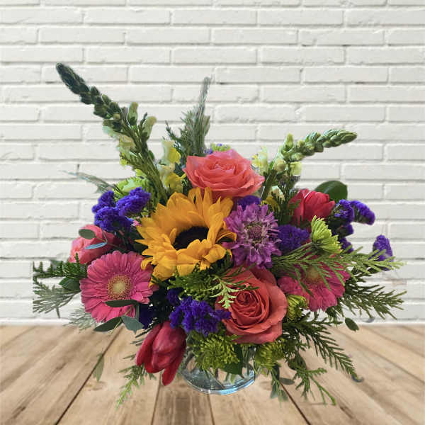 Colorful bouquet with sunflowers, roses, and gerbera daisies in a glass vase