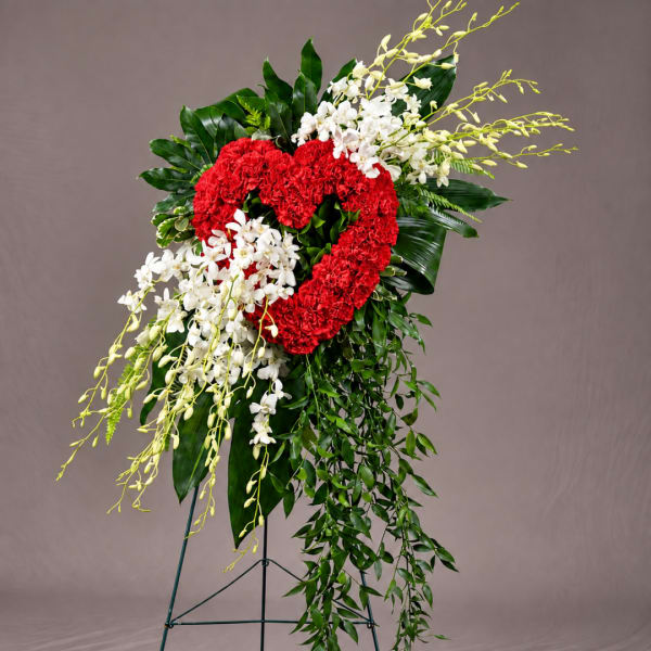 Heart-shaped red floral spray with white orchids and cascading greenery on a stand