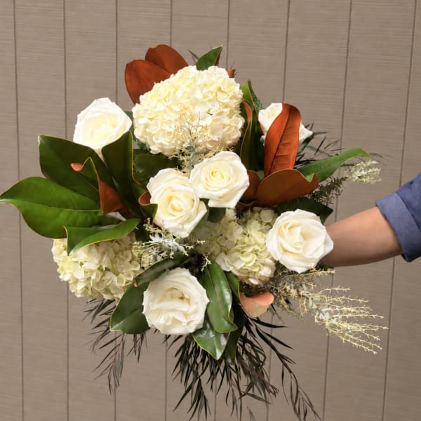 White roses and hydrangeas arranged with broad green and copper-toned foliage