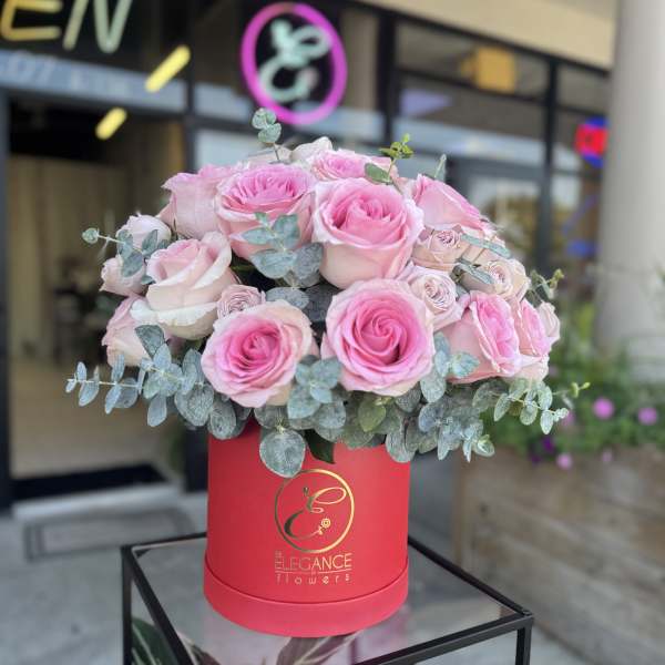 Pink roses arranged in a red hat box with eucalyptus