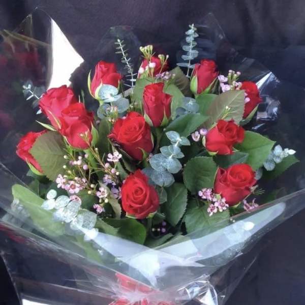 Bouquet of red roses with small pink filler flowers wrapped in clear cellophane with a red bow.