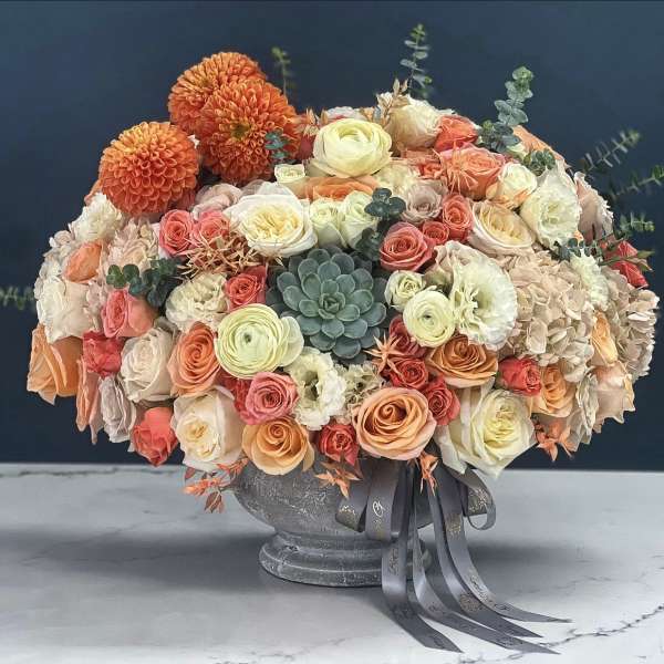 Mixed bouquet of peach, cream, and orange flowers in a gray vase