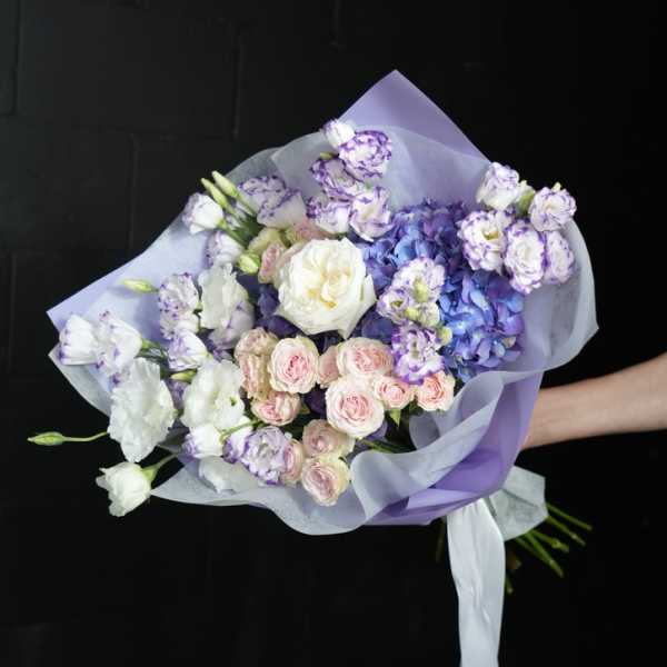 Hand-tied bouquet of purple, white, and pink flowers wrapped in lavender paper
