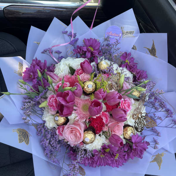 Round bouquet of pink and purple flowers with chocolates in lavender wrapping paper