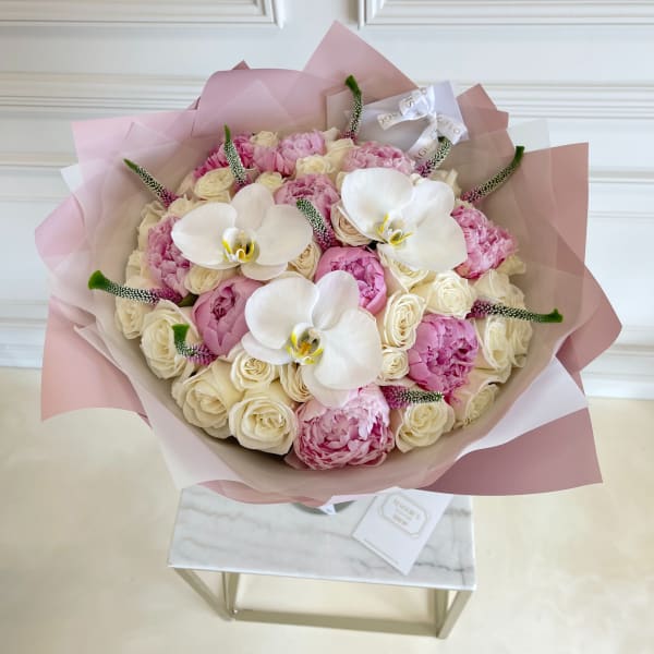 Bouquet of pink and cream flowers with white orchids wrapped in blush paper