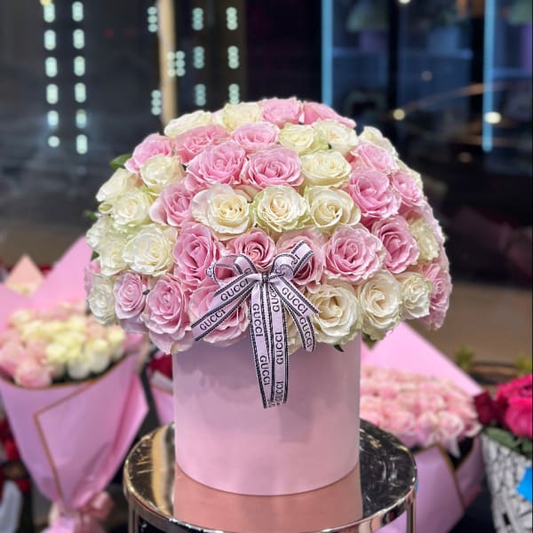 Pink and white roses arranged in a round hatbox with a ribbon bow