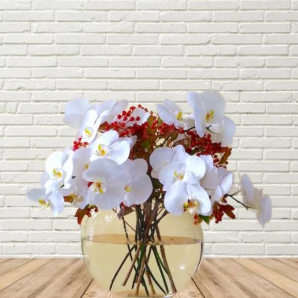 White orchid arrangement in a round glass vase with red berry accents