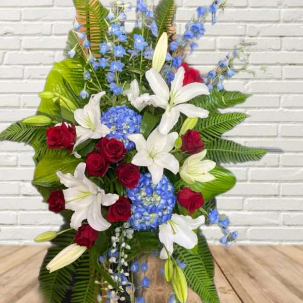 Standing floral spray with red roses, white lilies, and blue flowers