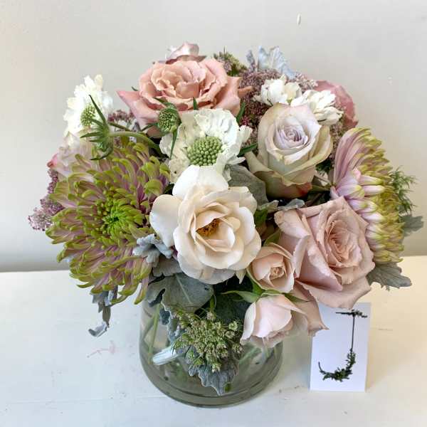 Pastel bouquet of roses, chrysanthemums, and white blooms in a glass vase