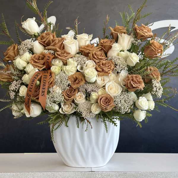 Large rose arrangement in a white vase with tan and white blooms