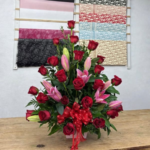 Red roses and pink lilies in a white vase with a red bow