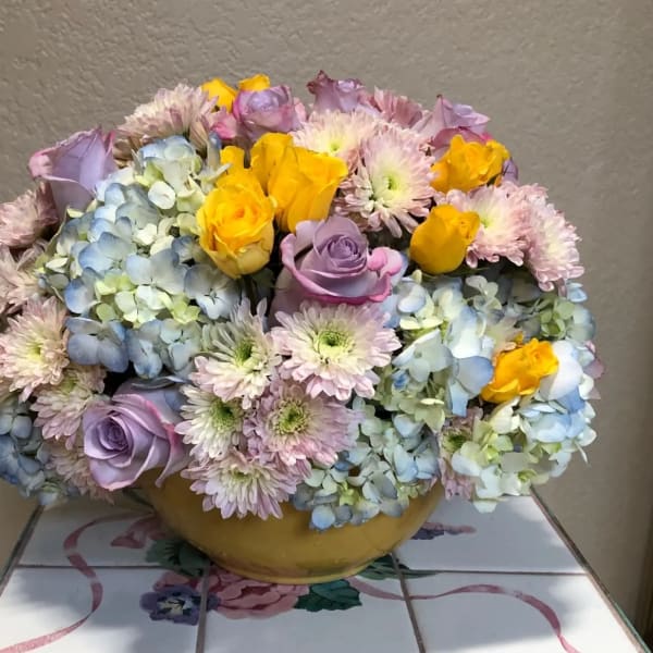 Pastel bouquet of roses, hydrangeas, and chrysanthemums in a yellow bowl vase