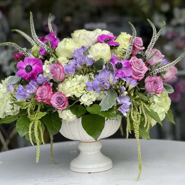 Pink and lavender flowers arranged in a white pedestal vase