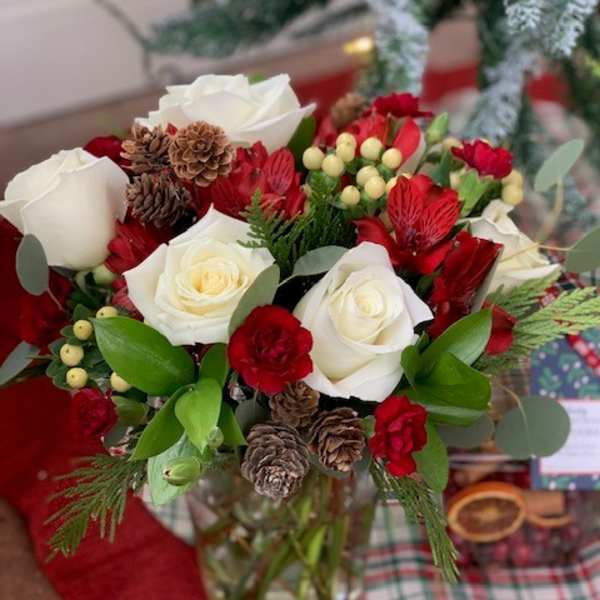 Red and white rose bouquet with pinecones in a glass vase