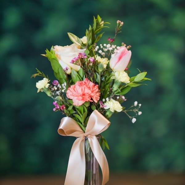 Pink and white bouquet in a tall glass vase with a satin ribbon