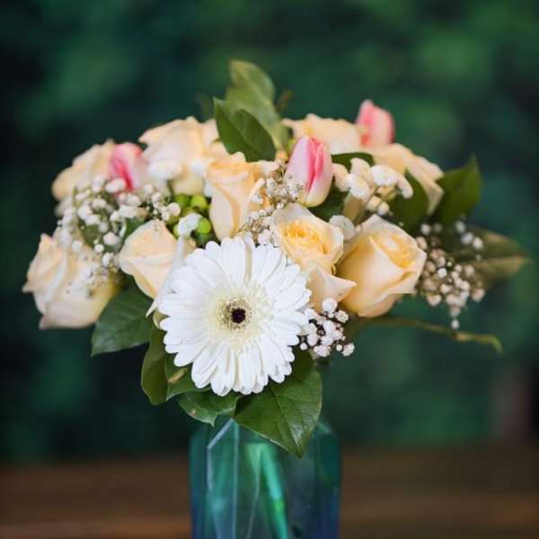 Bouquet of cream roses, pink tulips, and a white gerbera in a blue vase