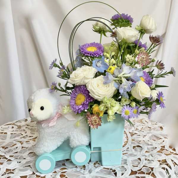 Pastel flower arrangement in a mint box beside a plush lamb on wheels