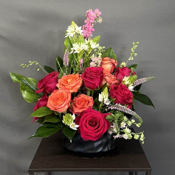 Mixed rose arrangement in a black vase with pink and orange blooms