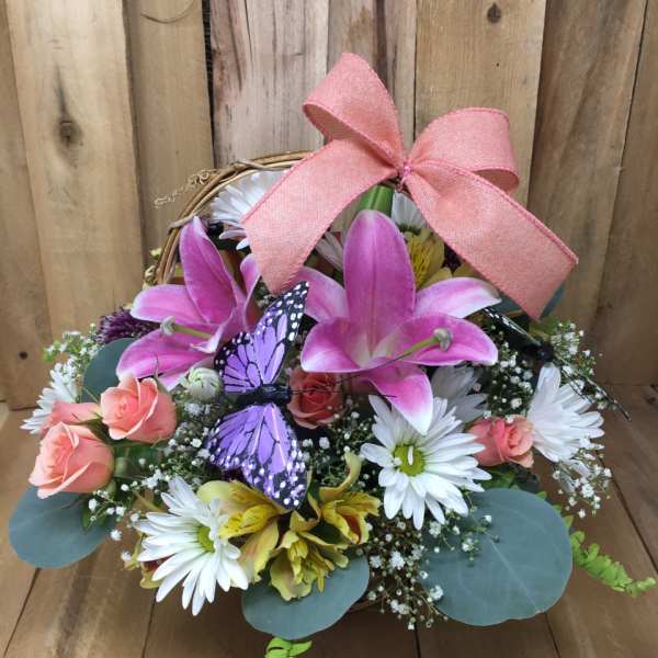 Basket arrangement with pink lilies, white daisies, and a pink bow