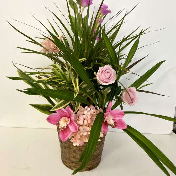 Pink orchids and roses in a woven basket with long green leaves