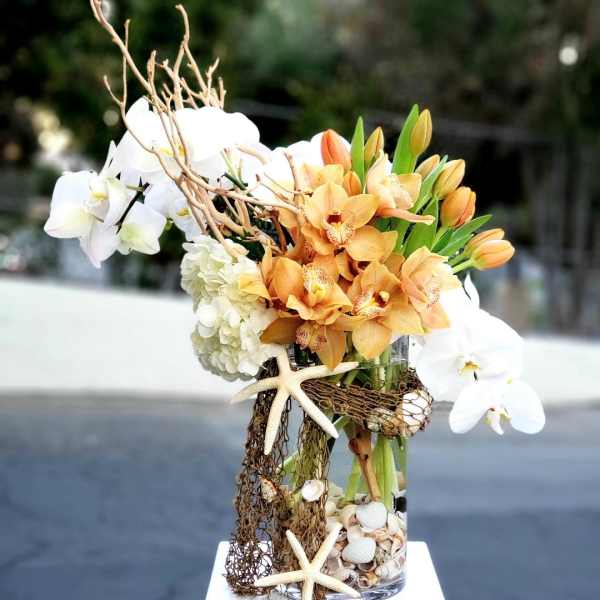 Orchid arrangement in a glass vase with starfish and shells