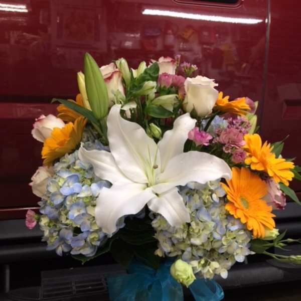 Bouquet with white lilies, blue hydrangeas, and orange daisies in a glass vase