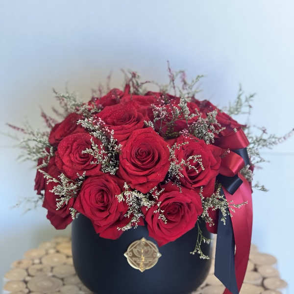 Red roses arranged in a black round box with ribbon