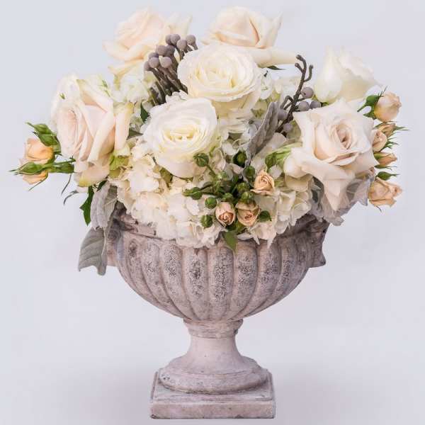 Cream roses and white flowers arranged in a stone urn
