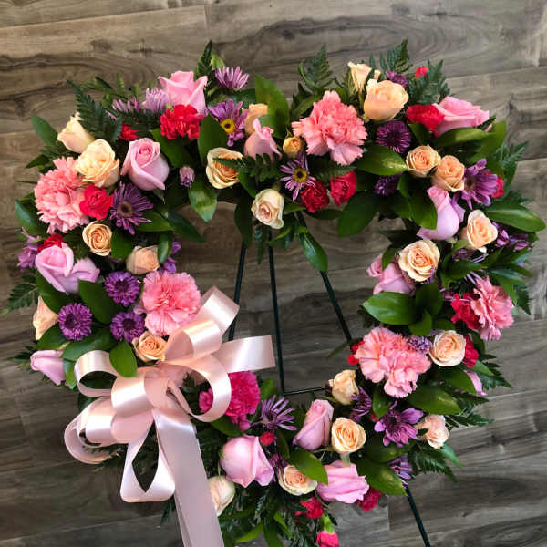 Heart-shaped floral wreath with pink, peach, and purple flowers on a stand