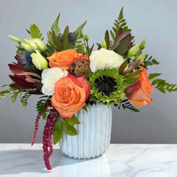 Orange roses and white carnations in a ribbed white vase