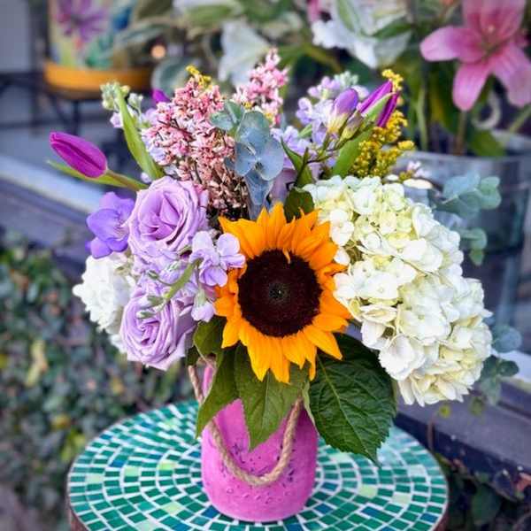 Mixed bouquet with a sunflower, lavender roses, and white hydrangeas in a pink vase