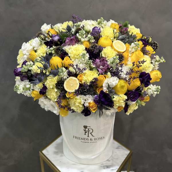 Large yellow, white, and purple flower arrangement in a white hatbox with lemon slices