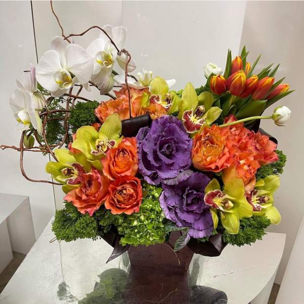 Colorful floral arrangement with orchids, roses, tulips, and purple cabbage in a dark vase