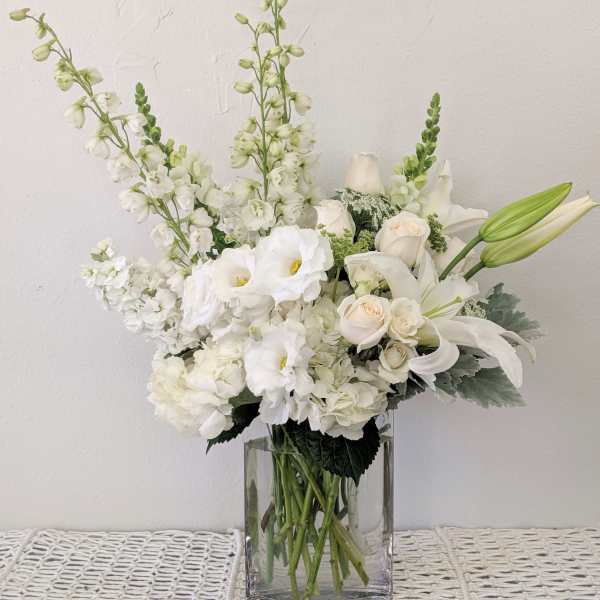 White floral arrangement in a clear glass vase with lilies and roses