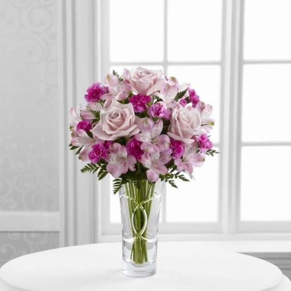 Pink and white bouquet of roses and small filler flowers in a clear glass vase