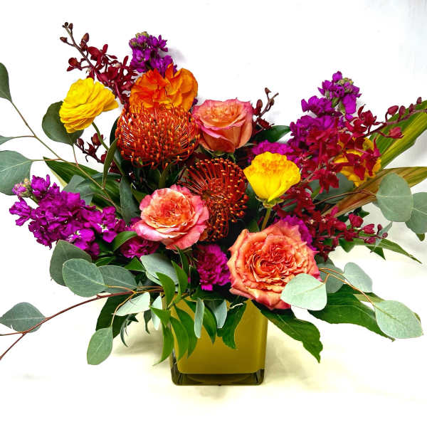 Mixed bouquet of orange, pink, yellow, and purple flowers in a square vase