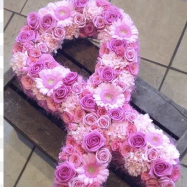 Pink floral arrangement shaped like an awareness ribbon on a wooden crate