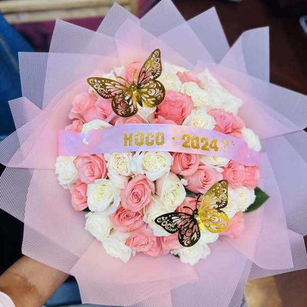 Round bouquet of pink and white roses wrapped in pink mesh with gold butterfly accents and HOCO 2024 ribbon.