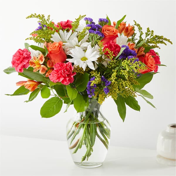 Mixed bouquet of roses, daisies, carnations, and alstroemeria in a glass vase