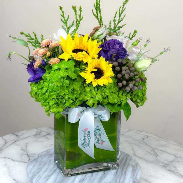 Bright mixed bouquet with sunflowers in a square glass vase