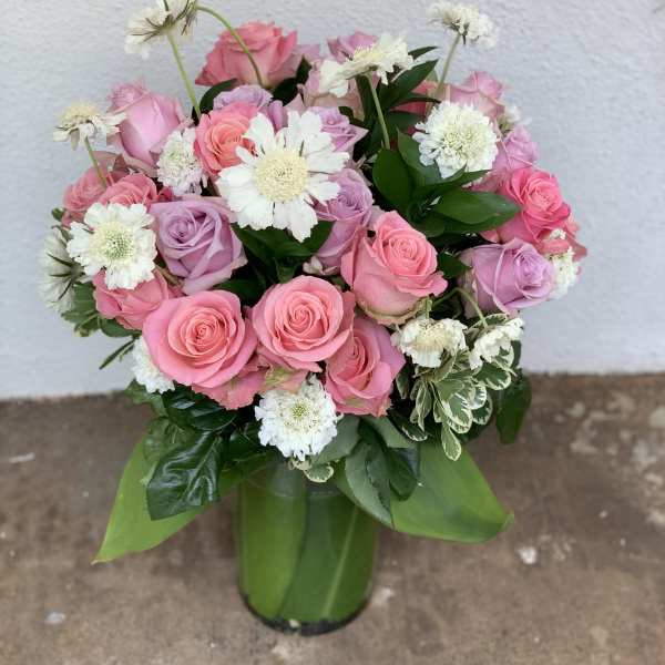 Pink and lavender roses arranged with white daisies in a green vase