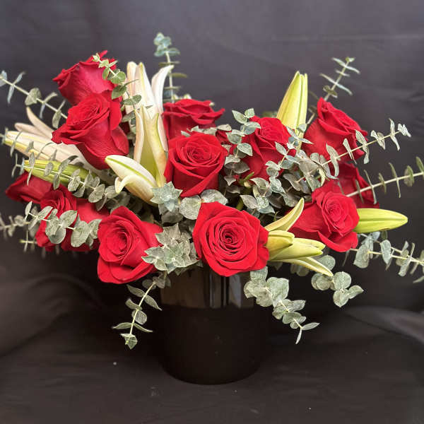 Red roses and white lilies in a black vase with trailing eucalyptus