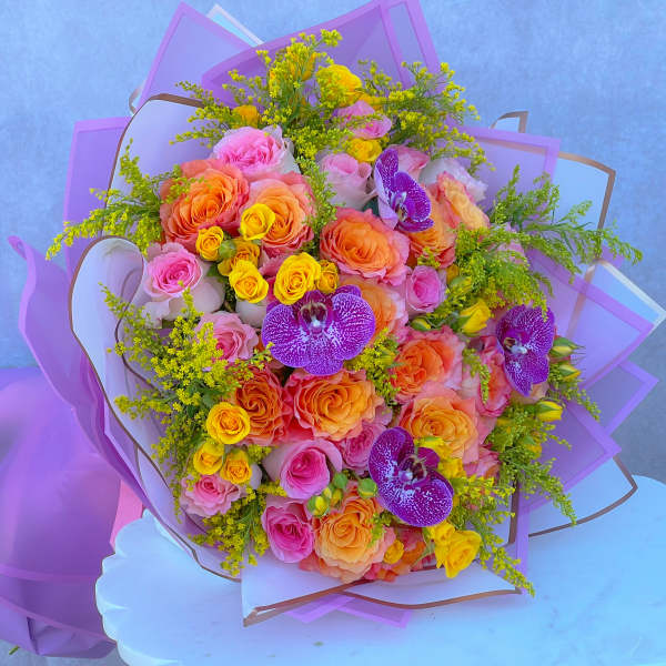 Large bouquet of pink, orange, and yellow roses with purple orchids wrapped in lavender paper.