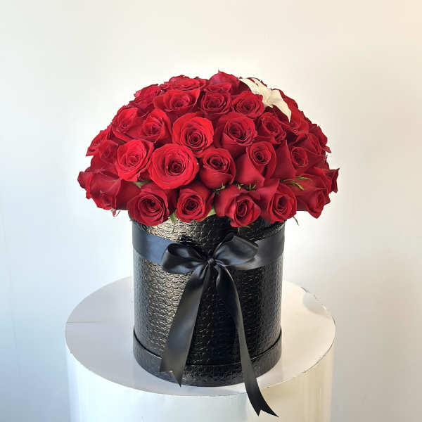 Red roses arranged in a black round box with a ribbon bow