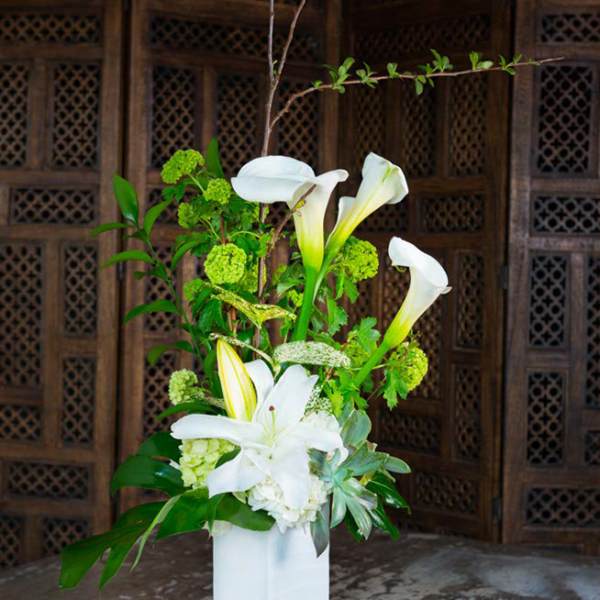 Tall white floral arrangement with calla lilies and lilies in a white vase