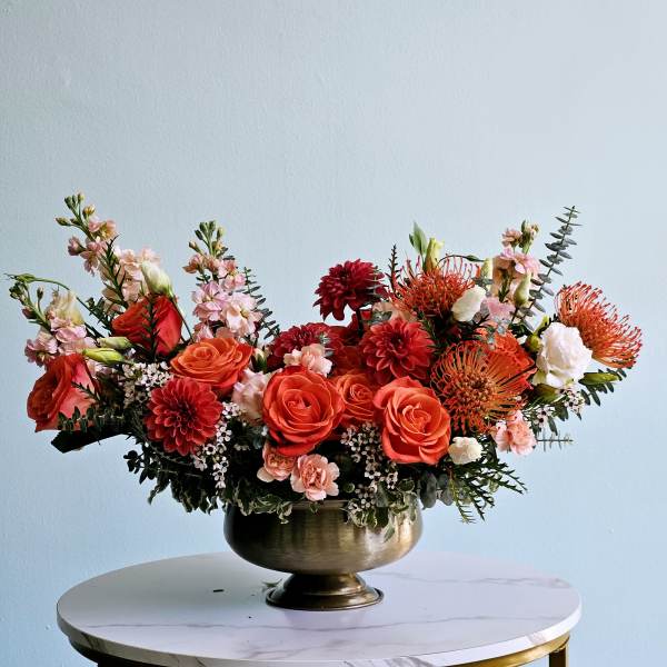 Orange and red floral arrangement in a brass bowl vase