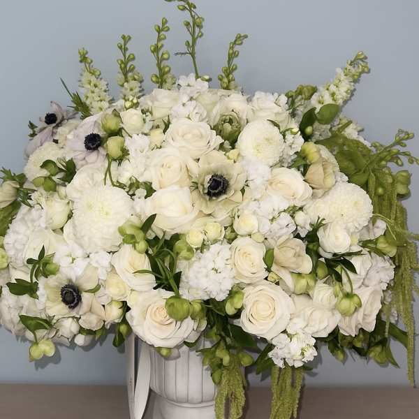 White floral arrangement in a white urn vase with trailing green accents