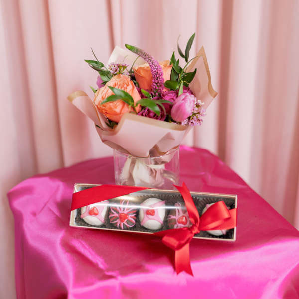 Pink and peach bouquet in a glass vase with a box of chocolates