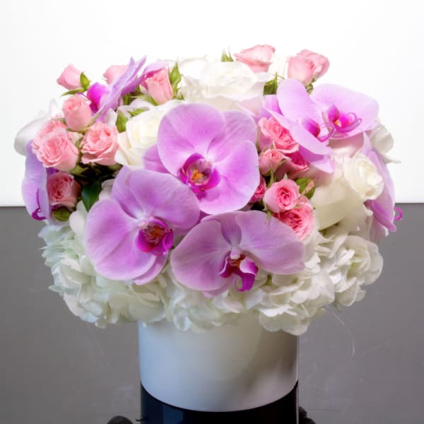 Pink and white floral arrangement with orchids and roses in a white vase