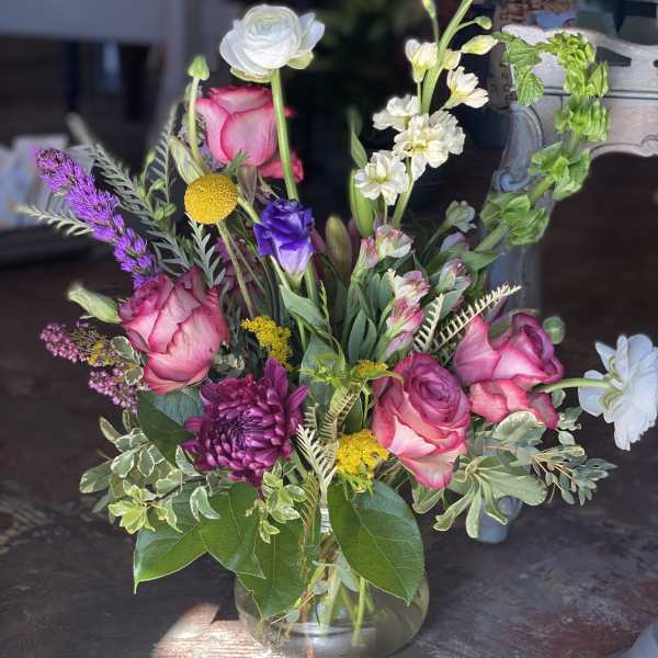 Mixed bouquet of pink roses, white blooms, and purple flowers in a glass vase